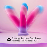 Displayed against a pink and purple gradient background is the Avant Borealis Dreams - Cotton Candy Realistic Dildo, an artisanal piece by Avant featuring a vibrant color palette. The text highlights its "Strong Suction Cup Base for Hands-Free Pleasure & Play." Crafted from platinum-cured silicone, this dildo is also harness compatible for versatile enjoyment.